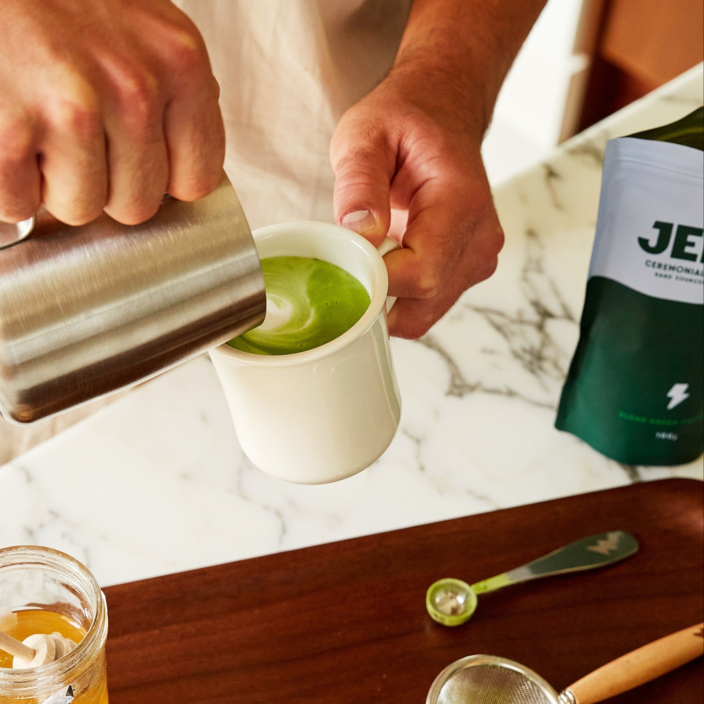 Person making a green tea latte with a pouch of JENKI in the background