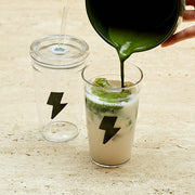 Green liquid being poured into a glass with a lightning bolt symbol on a wooden surface